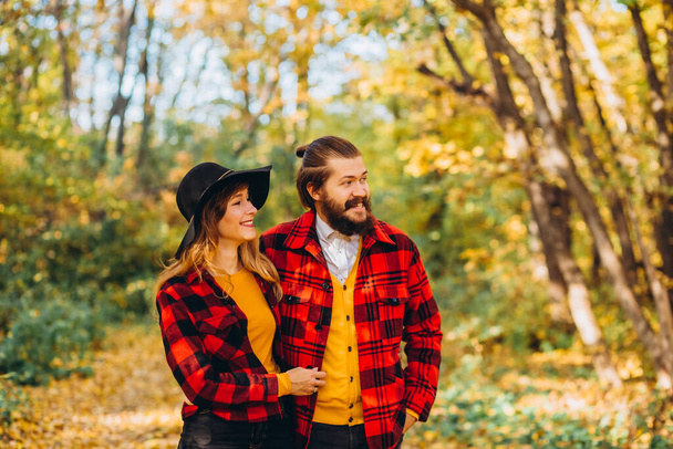 Erkek ve kız sonbahar ormanında yürüyorlar. Doğadaki neşeli genç bir çiftin yakın plan portresi. Sarı ormanda kırmızı ceketli şık giyinmiş bir adam ve kadın.. - Fotoğraf, Görsel