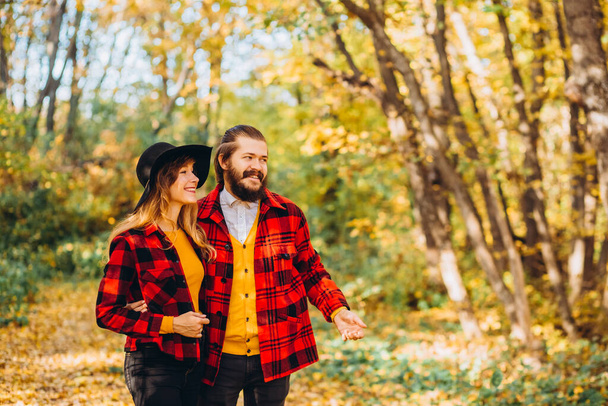 男と女が秋の森を歩いてる。自然界で明るい若いカップルのクローズアップ肖像画。黄色の森の中で赤いジャケットでスタイリッシュな服を着た男と女. - 写真・画像