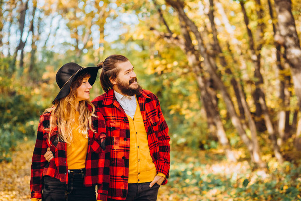 Άντρας και κορίτσι περπατούν στο φθινοπωρινό δάσος. Κοντινό πορτρέτο ενός χαρούμενου νεαρού ζευγαριού στη φύση. Κομψά ντυμένος άντρας και γυναίκα με κόκκινα μπουφάν σε ένα κίτρινο δάσος. - Φωτογραφία, εικόνα