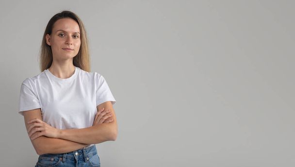 confident beautiful young european woman with arms crossed, white t-shirt, looking calmly at camera, successful woman posing studio - Фото, изображение