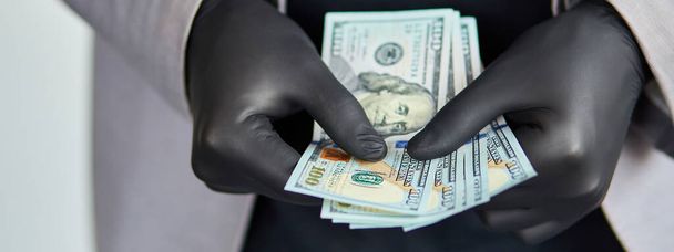 Un uomo che tiene in mano i soldi con i guanti medici neri. Crisi del coronavirus. Risparmiare. - Foto, immagini