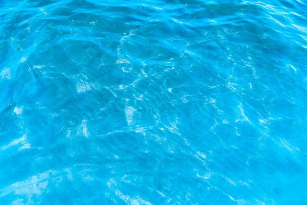 Modrá transparentní mořská voda v blízkosti pláže textury pozadí. průzračný vodní povrch s mírnými vlnami a oslnivým světlem za slunečného dne - Fotografie, Obrázek