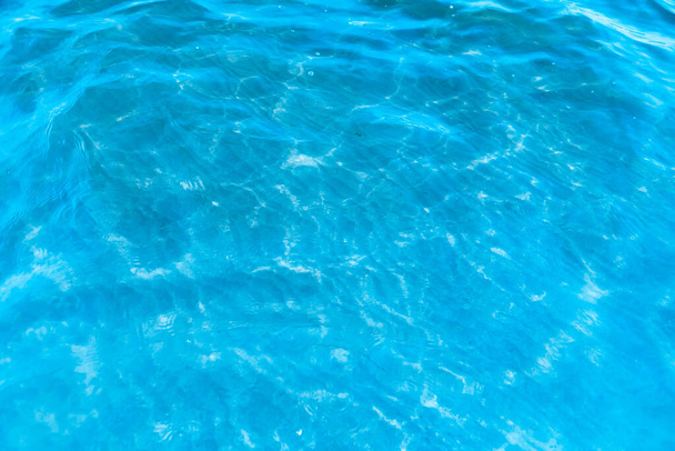 Modrá transparentní mořská voda v blízkosti pláže textury pozadí. průzračný vodní povrch s mírnými vlnami a oslnivým světlem za slunečného dne - Fotografie, Obrázek