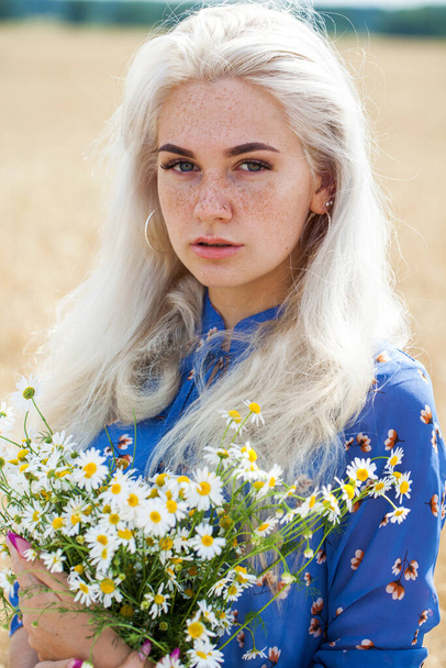 close up portrait of a young blonde girl with a bouquet of chamomile in a field - Fotó, kép