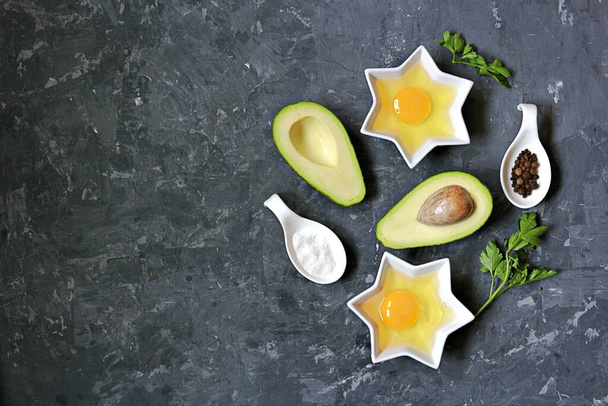 Ingredients for cooking baked avocado with egg on a dark concrete background: ripe avocado, cut in half, eggs, salt, pepper, parsley. Top view, copy space. - Photo, Image