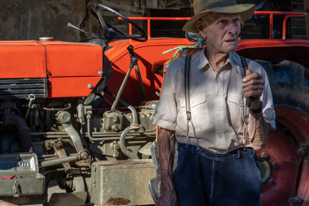 Портрет дуже старого фермера з солом'яним капелюхом, що пояснює життя перед червоним трактором. Реальний ретро, Крупним планом
. - Фото, зображення