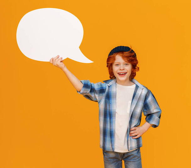 Happy stylish boy with hand on waist smiling and holding blank speech balloon near head against yellow backgroun - Foto, Imagen