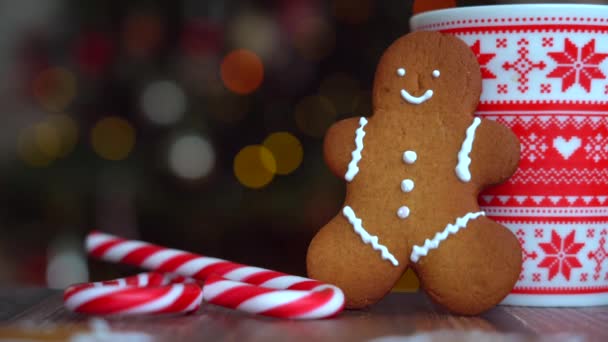 Christmas video with gingerbread man red mug with christmas ornament on light bokeh from Xmas tree and red striped holidays candies. Xmas candies and cup with marshmallow on wood background. 4k video - Footage, Video