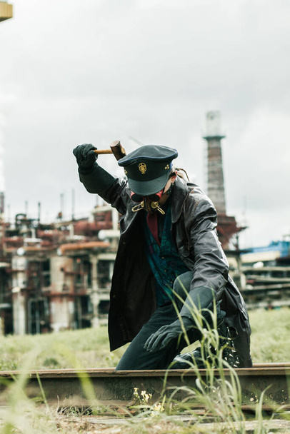 Fiatalember kalapáccsal viselte steampunk stílusban dolgozik vasút közelében gyár - Fotó, kép