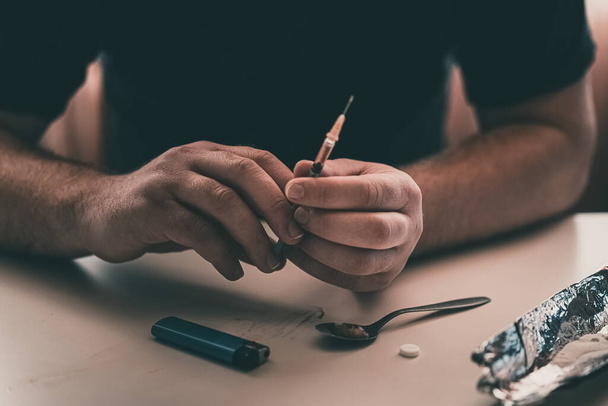 Addict at the table with a syringe heroin methamphetamine addiction - 写真・画像