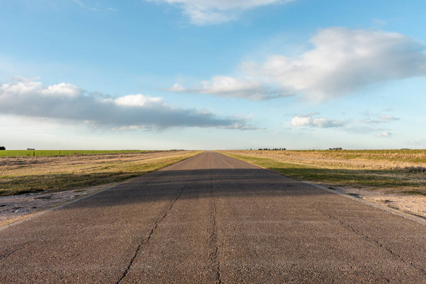 Kırsal bölgedeki tarımsal alanlardan geçen boş asfalt yolu. Gün batımında yumuşak bulutlu açık mavi gökyüzü.. - Fotoğraf, Görsel