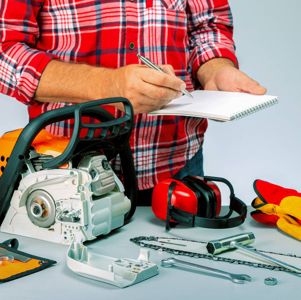 Man repairing a chainsaw in workbench . Workman holding nootebook and pen. Price list of repair chainsaw. Small business. - Φωτογραφία, εικόνα