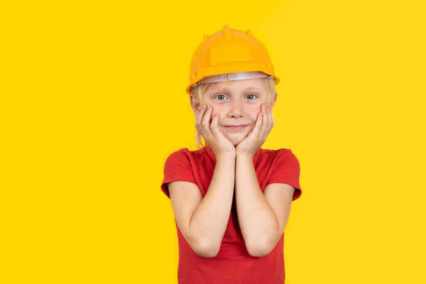 Cute fair-haired boy in protective orange helmet on yellow background - Photo, Image