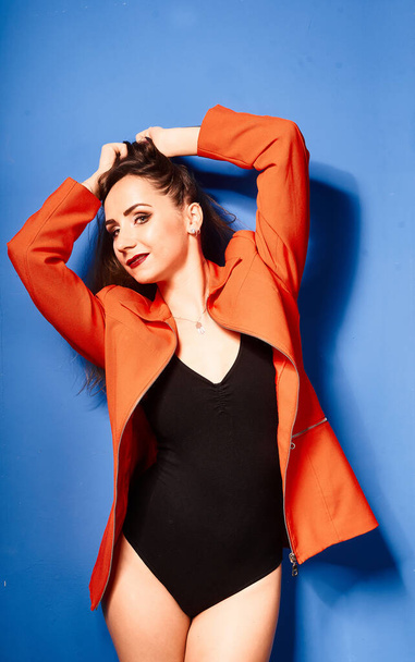  NIce young white girl, wearing black body and orange jacket, blue background     , very contrasted picture           - Zdjęcie, obraz