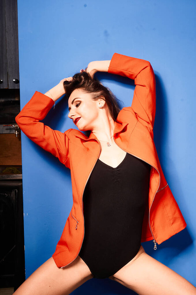  NIce young white girl, wearing black body and orange jacket, blue background     , very contrasted picture           - Foto, Imagen