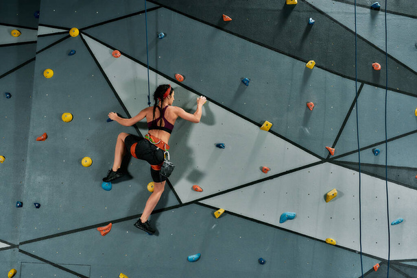 Woman in safety equipment and harness training on the artificial climbing wall indoors - Fotó, kép