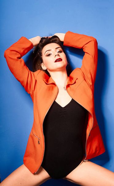  NIce young white girl, wearing black body and orange jacket, blue background     , very contrasted picture           - Fotoğraf, Görsel