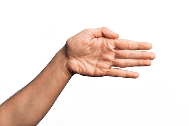 Hand of caucasian young man showing fingers over isolated white background stretching and reaching with open hand for handshake, showing palm - Photo, Image