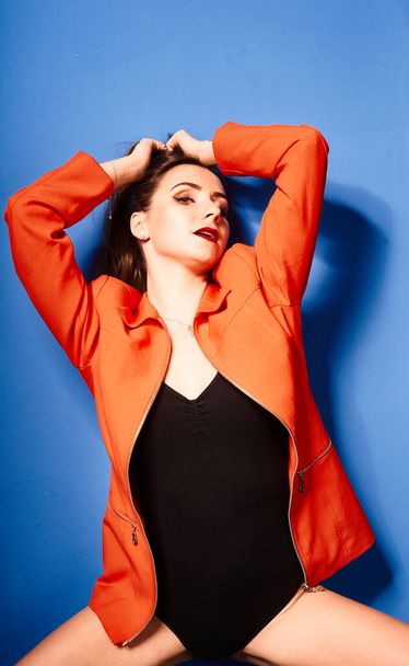  NIce young white girl, wearing black body and orange jacket, blue background     , very contrasted picture           - Foto, Imagem