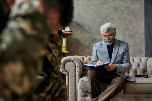立ち上がるプロセス。成熟した心理学者は、軍人と通信し、治療セッション中に注意を払う。うつ病、精神的外傷に苦しむ兵士。PTSDの概念 - 写真・画像
