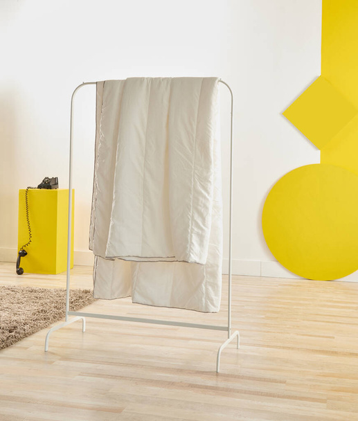 Bílá deka visí v místnosti, bílé a žluté pozadí, kulatý dřevěný styl a konferenční stolek. - Fotografie, Obrázek