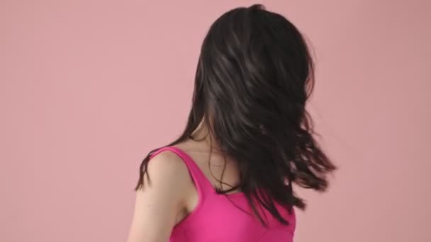 A smiling young woman is shaking her hair isolated over a pink background - Πλάνα, βίντεο