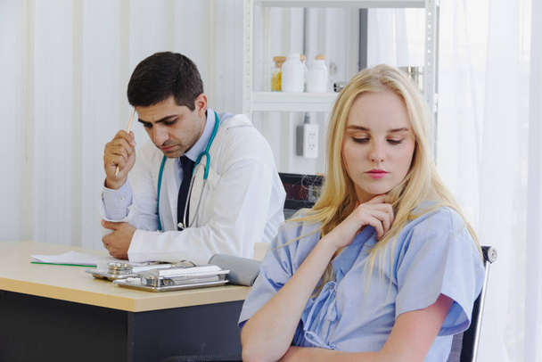 Stationäre Patientin sitzt mit einem männlichen Arzt auf einem Stuhl im Behandlungszimmer und denkt über ihr Symptom nach - Foto, Bild