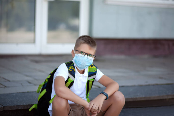 Takaisin kouluun. Shoolboy lasit yllään naamio ja reput suojaavat ja turvallisuutta koronavirus. Lapsi menee kouluun pandemian jälkeen. Seisomassa koulun lähellä. opiskelijat ovat valmiita uuteen vuoteen. - Valokuva, kuva