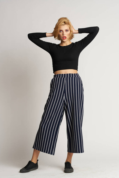 Pretty woman in black sweater striped pants fashion clothes light background studio - Foto, imagen