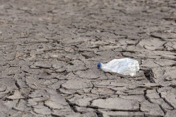 порожня крихка пластикова пляшка на сухій тріснутій пустелі, як сірий фон
 - Фото, зображення