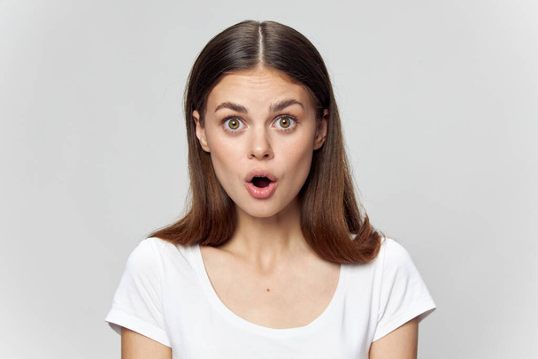 Surprised woman with open mouth in a white t-shirt on an isolated background close-up  - Фото, зображення