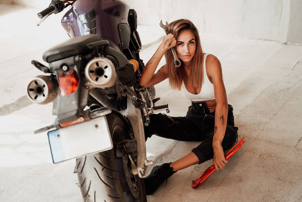 Vrouwelijke leuke technicus en moderne sport motorfiets in lichte garage - Foto, afbeelding