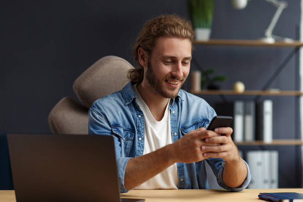 Young man using smartphone and smiling. Happy businessman using mobile phone apps, texting message, browsing internet, looking at smartphone. Concept of young people working with mobile devices - Photo, Image
