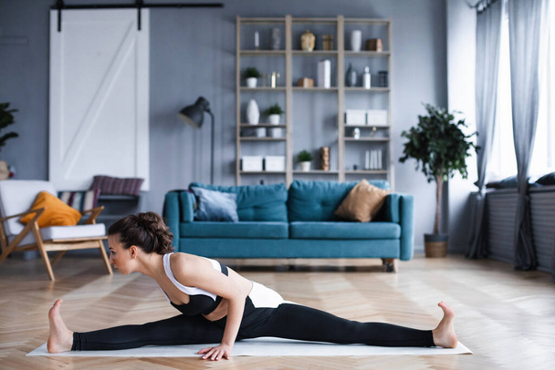 Young woman doing stretching exercise at home. Practicing yoga, working out indoor full length. - Foto, immagini