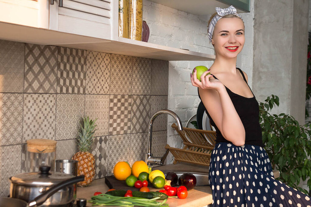 Girl in pin-up style in the kitchen with an apple in hand - Photo, Image