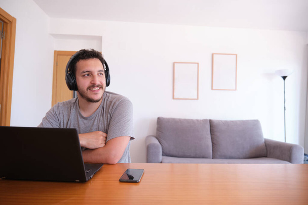 Young man wearing headphones watching series, videos, online classes on a laptop with the fan on. Studying online and e-learning concept. - Photo, Image