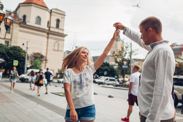 Νέοι ερωτευμένοι περπατούν στο παλιό κέντρο της πόλης Lviv φορώντας παραδοσιακά ουκρανικά πουκάμισα. Μερικοί χοροί διασκεδάζουν. - Φωτογραφία, εικόνα