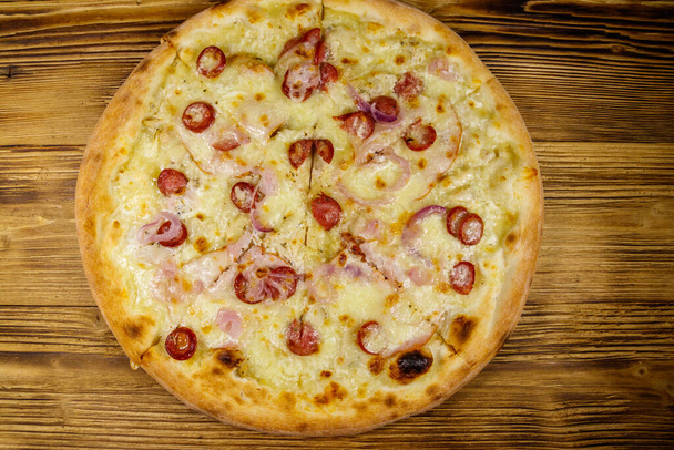 Pyszna, świeża pizza z kiełbasą, czerwoną cebulą i serem na drewnianym stole. Widok z góry - Zdjęcie, obraz