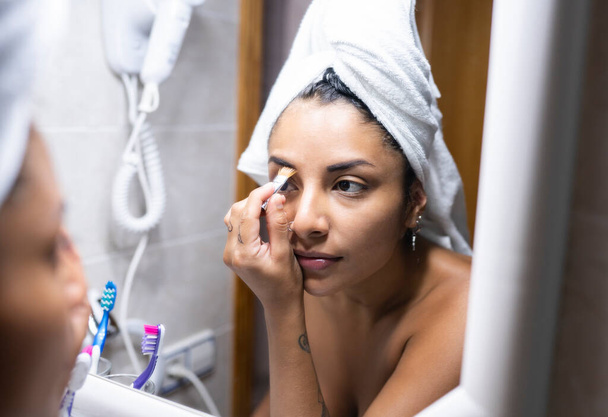 Nainen, jolla on pyyhe hiuksissa laittaa meikki peilin edessä - Valokuva, kuva