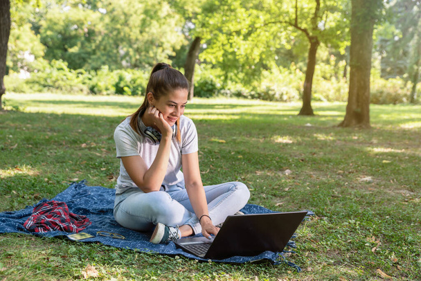Girl sitting in the park and surfing the internet on her laptop computer - Фото, зображення