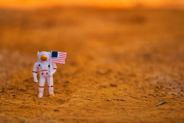 Toy astronaut on a natural red soil simulating the planet Mars with the Usa flag. - Φωτογραφία, εικόνα