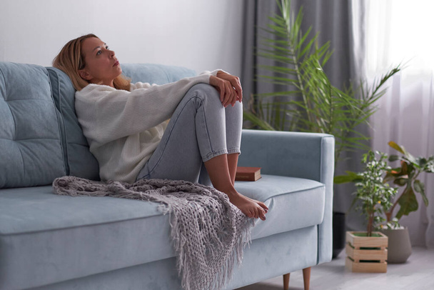 Sad woman sitting on a sofa in the living room. Frustrated confused female feels unhappy problem in personal life quarrel break up with boyfriend - Valokuva, kuva