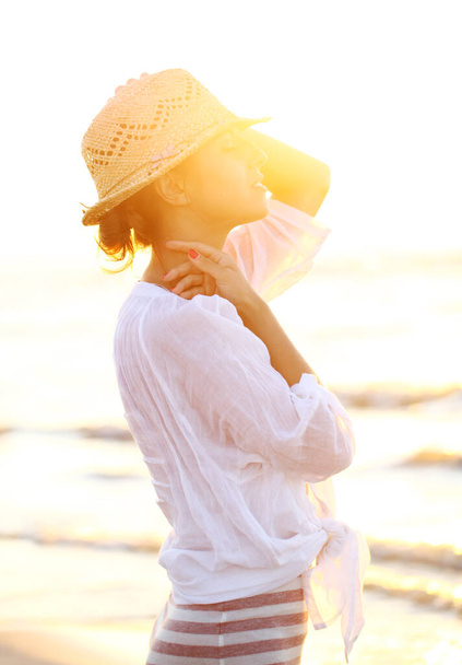 Νέα και όμορφη γυναίκα φορώντας καπέλο στο φως του ηλιοβασιλέματος - Φωτογραφία, εικόνα