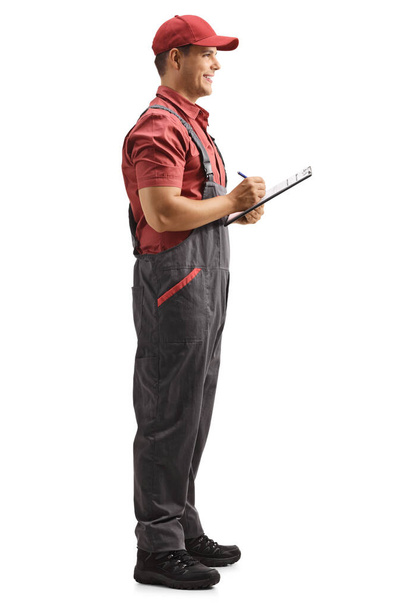 Full length profile shot of a male worker in a uniform writing a document isolated on white background - Φωτογραφία, εικόνα