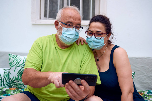 Una coppia anziana con maschere chirurgiche durante l'utilizzo di un telefono cellulare. Anziani - Foto, immagini