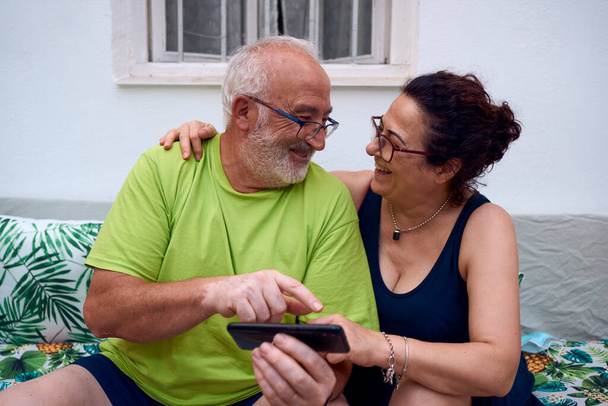 Una pareja de ancianos riendo mientras usa un teléfono móvil. Concepto pareja mayor - Foto, imagen