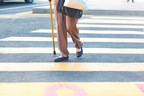 Een oude vrouw met een stok gaat de straat over. - Foto, afbeelding