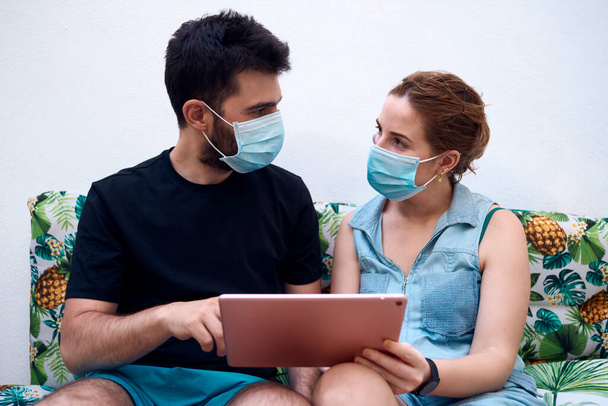 Um casal com máscaras cirúrgicas escolhendo um destino de férias usando um tablet. Conceito de férias - Foto, Imagem