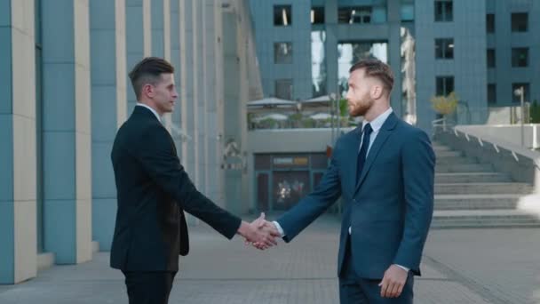Two business men shake hands when meeting, agree to a deal or say hello. Portrait of handshake of two successful businessmen making a deal. Office building on the background. Business district. - Footage, Video