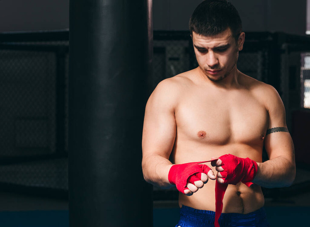 Young boxer wrapping his hands with red elastic bandage preparing to workout - Фото, зображення
